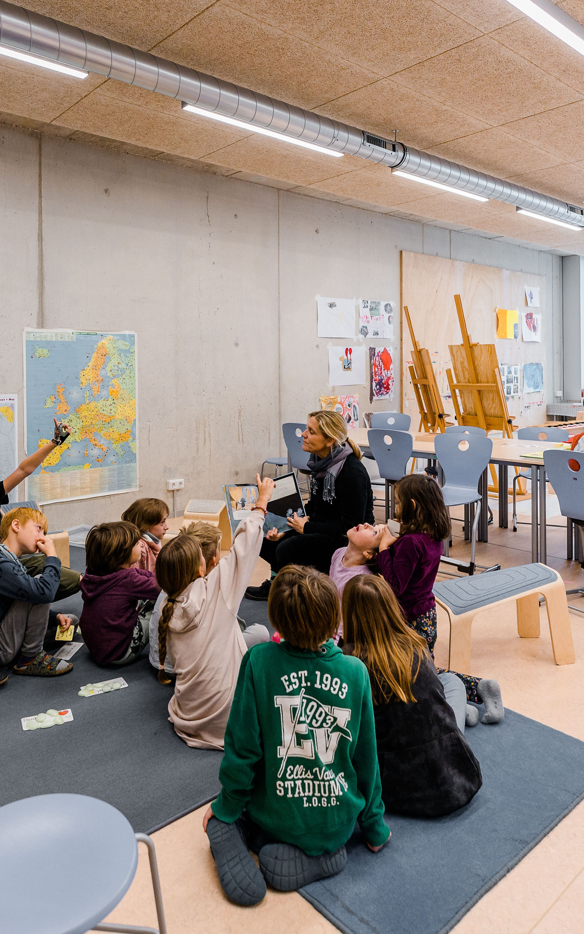 Innenperspektive mit sitzenden Schüler:innen in ihrer Lerngruppe, die aufmerksam der Lehrerin zuhören.