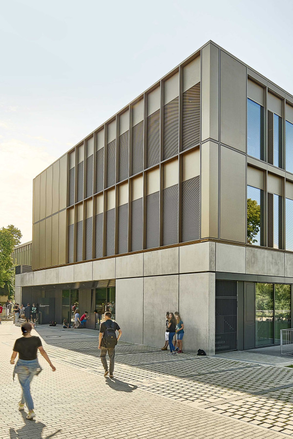 Außenperspektive von der dreigeschossigen Schule mit einem bespielten Schulhof im Hintergrund.